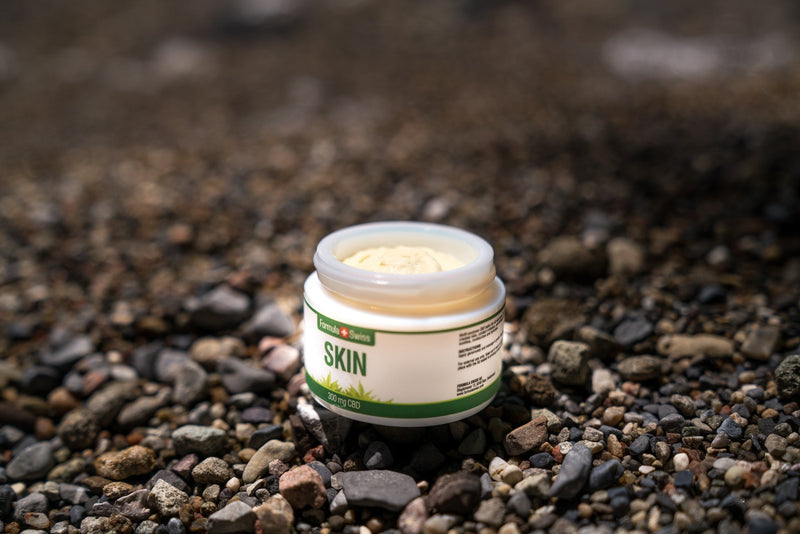 Öppnad burk Formula Swiss CBD Skin-balsam, 300 mg CBD, på en stenstrand