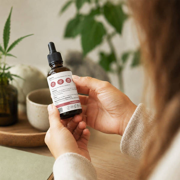 Kvinna som granskar produktetiketten på en cannabinoidolja från Formula Swiss i en naturlig inomhusmiljö.